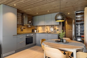 Una cucina moderna con mobili grigi, soffitto in legno e zona pranzo con tavolo e sedie.