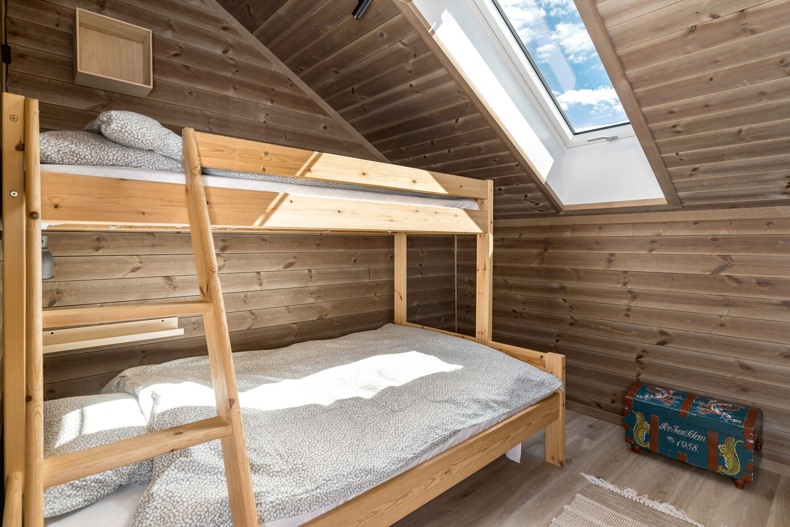 A bunk bed in a wooden room with a skylight and a vintage trunk.