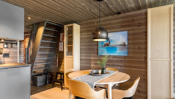A modern kitchen with a wooden interior, a dining area with a table and chairs, and a staircase leading to an upper level. - Modern apartment in Glomsrud Golsfjellet west (Gol)