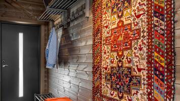 A room with a bench, a woven bench, a large patterned rug, and a door.