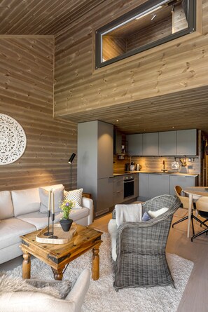 Un interior moderno con techo de madera, un sofá, una silla de mimbre, una mesa de centro y una zona de cocina.