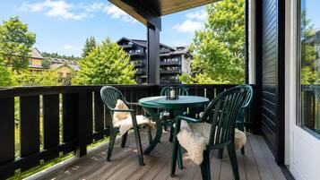 Een overdekt terras met een houten dek, een ronde tafel en vier stoelen.