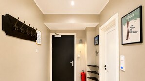 Un couloir avec une porte noire, un porte-manteau, un extincteur et un panneau encadré accroché au mur.