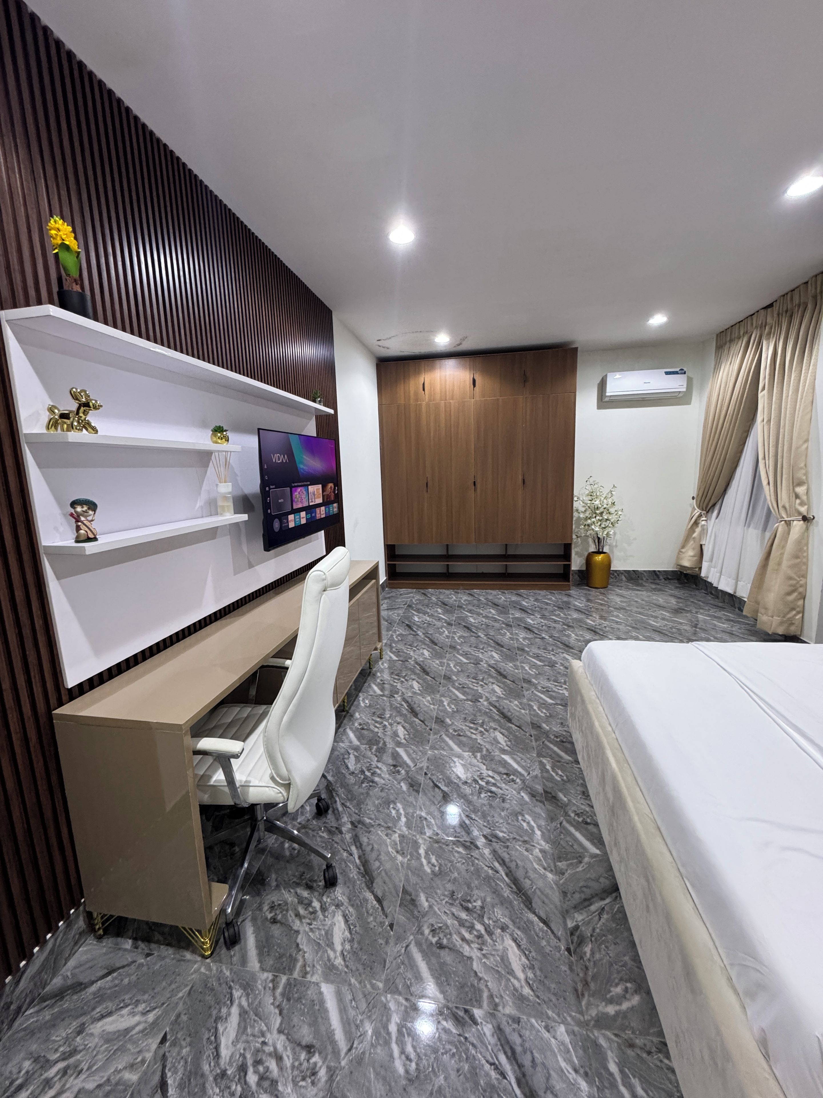 A modern bedroom with a bed, a desk with a chair, a wardrobe, and a TV.