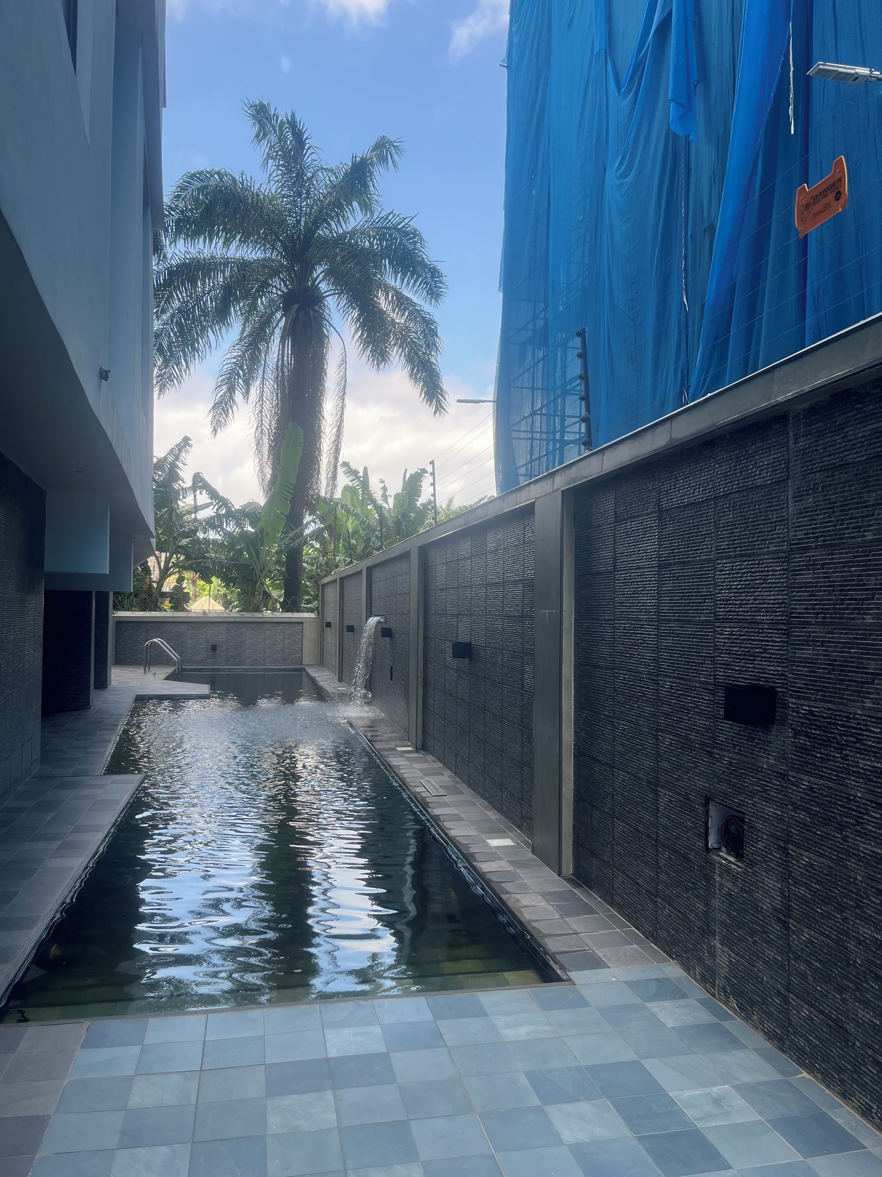 A modern building with a water feature, a palm tree, and a blue construction tarp.