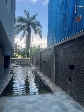 A modern building with a water feature, a palm tree, and a blue construction tarp. - Martins court (Lagos)