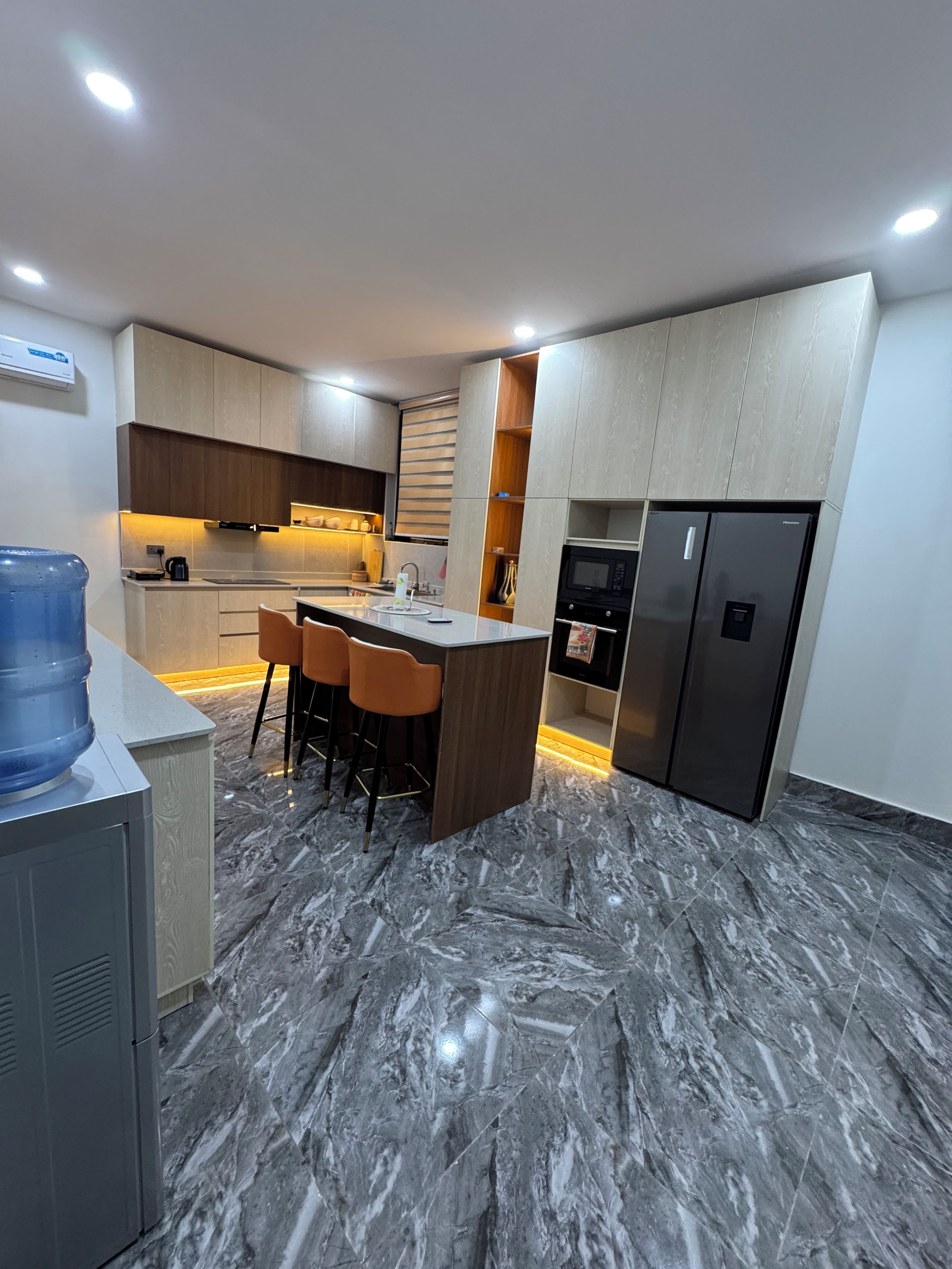 A modern kitchen with marble flooring, a built-in island with bar stools, and stainless steel appliances.