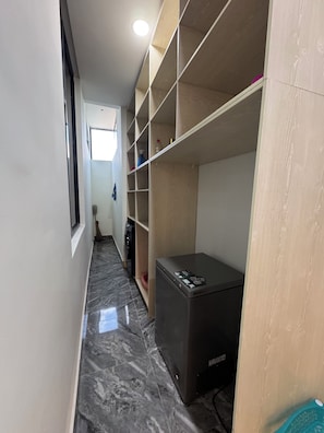 A narrow hallway with a marble floor, a refrigerator, and a wooden shelving unit. - Martins court (Lagos)