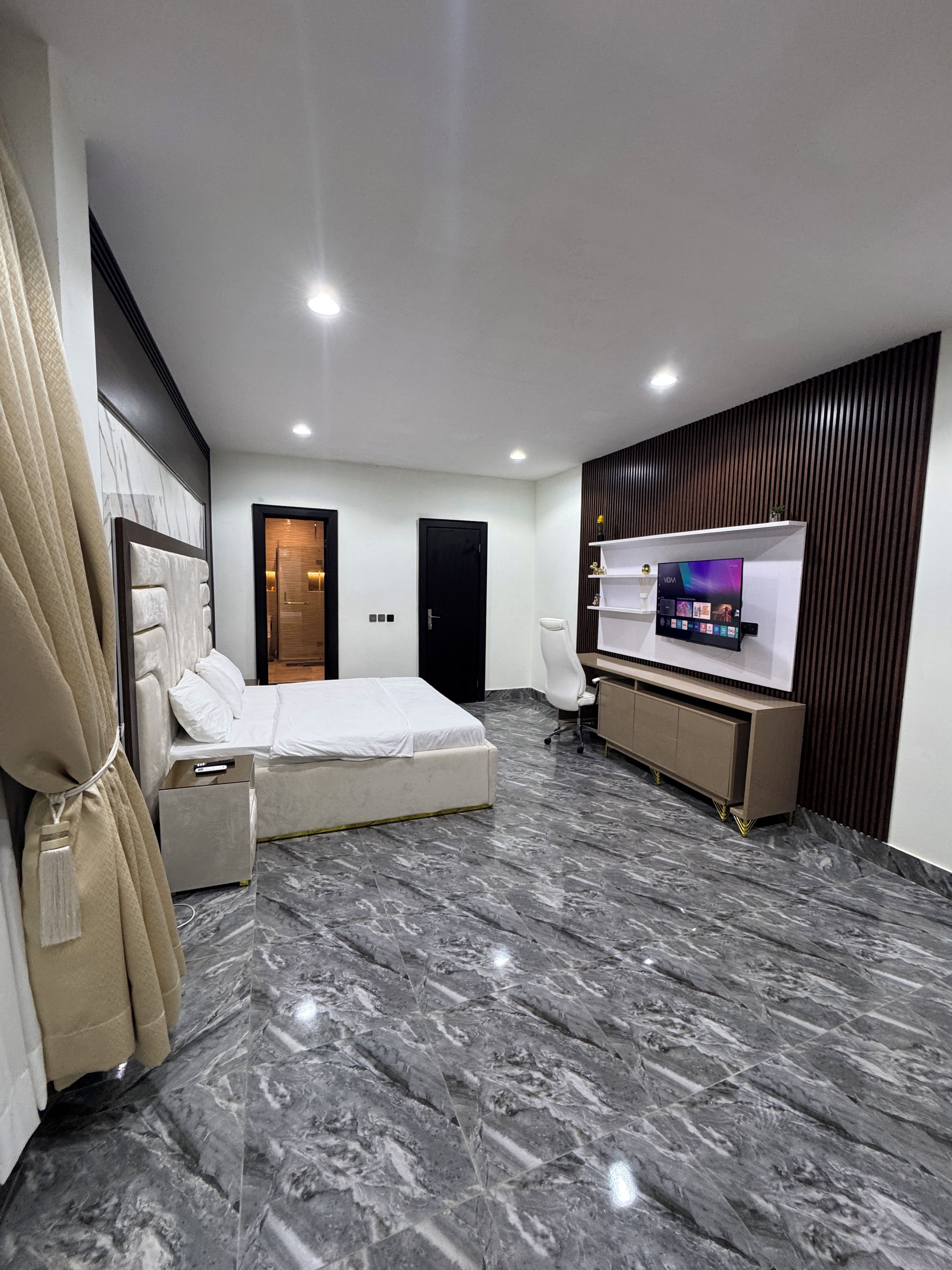 A modern hotel room with a bed, a TV, a desk, and a bathroom.