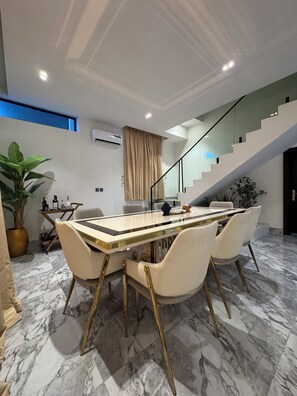 Un comedor moderno con suelo de mármol, una mesa con cubierta de vidrio y cuatro sillas con patas doradas.