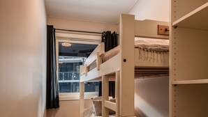 Een slaapkamer met een stapelbed, een raam, een kamerbreed tapijt met patroon en een houten vloer.