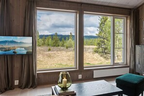 Et værelse med store vinduer, et fladskærms-tv, et bord med et stearinlys og en grøn skammel.