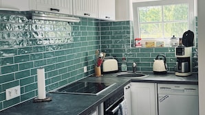 Uma cozinha moderna com armários brancos, painel de parede verde e uma janela que traz luz natural.