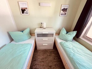 A room with two single beds, a bedside table with a lamp, and framed pictures on the wall.