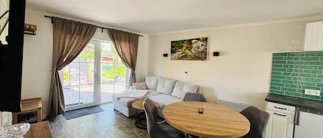 Een moderne woonkamer met een bank, een ronde houten tafel en een keuken met groene tegels.