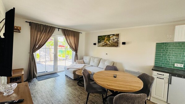A modern living room with a sofa, a round wooden table, and a kitchen area with green tiles.