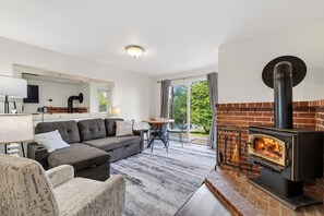 Una sala de estar moderna con chimenea, un sofá, una mesa de comedor y vistas a través de un ventanal.