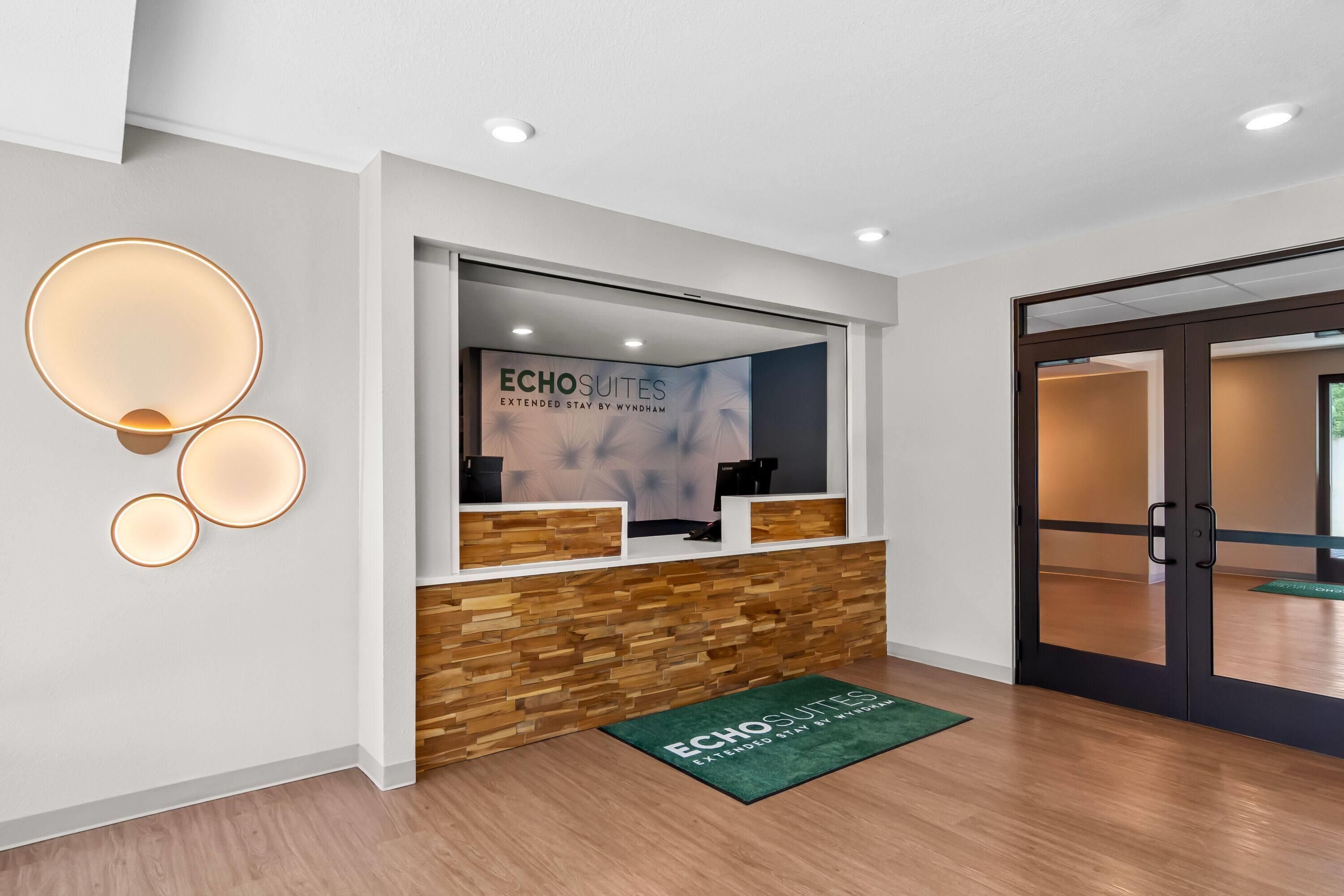 Un mostrador de recepción con un cartel de ECHO SUITES, paneles de madera y un tapete verde con el nombre del hotel.