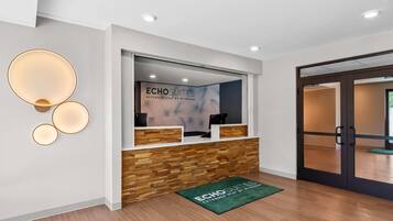 Un mostrador de recepción con un cartel de ECHO SUITES, paneles de madera y un tapete verde con el nombre del hotel.