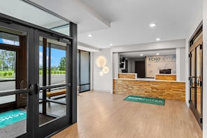 Ein Hotel-Rezeptionsbereich mit einer Rezeption, einer Wandleuchte und einer grünen Matte auf dem Boden.
