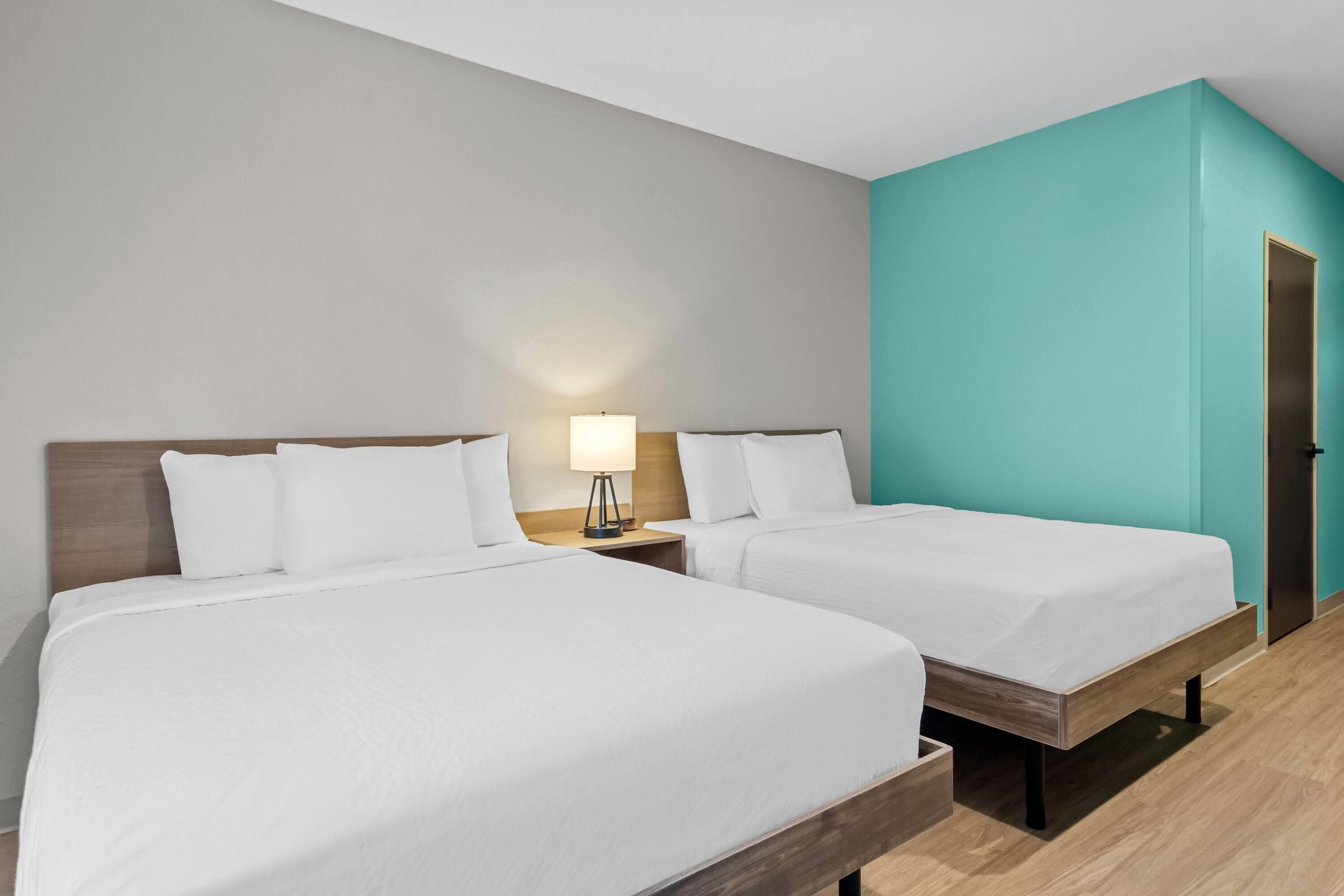 Camera d'albergo con due letti, un comodino con lampada e una parete verde acqua.
