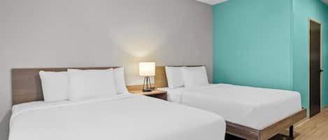 A hotel room with two beds, a nightstand with a lamp, and a teal accent wall.