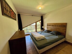 Ein Schlafzimmer mit Holzkopfstütze, einem Bett mit grüner Bettwäsche, einem Nachttisch mit Lampe und Blick auf einen Balkon.
