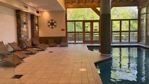 Ein Innenpool mit Fliesenboden, Liegestühlen, einer Steinwand und großen Fenstern.