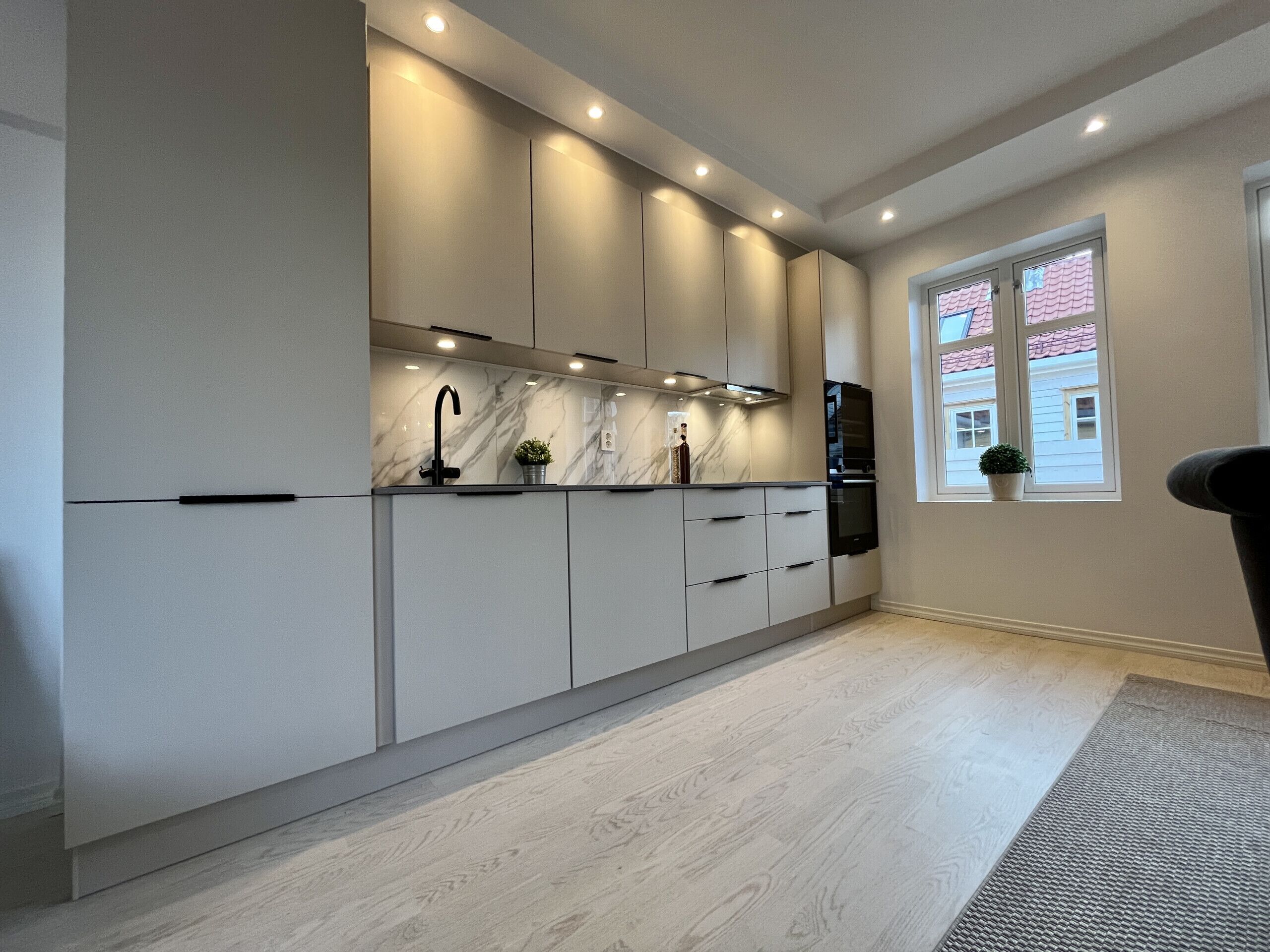 Eine moderne Küche mit eingebauten Schränken, einer Marmor-Spritzschutzwand und einem Fenster mit Blick auf ein Haus.