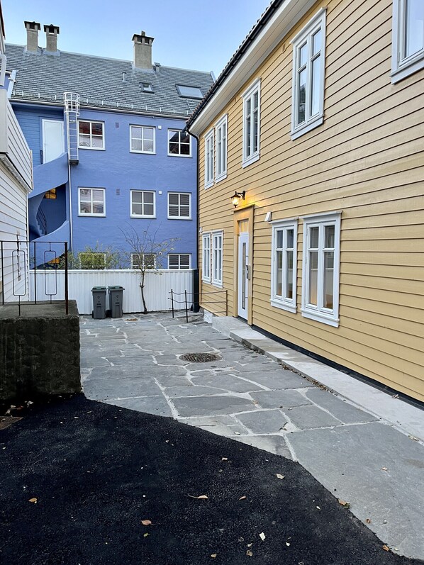 En innergård med stenbeläggning, en blå byggnad med en spiraltrappa och en gul byggnad med en dörr och fönster.