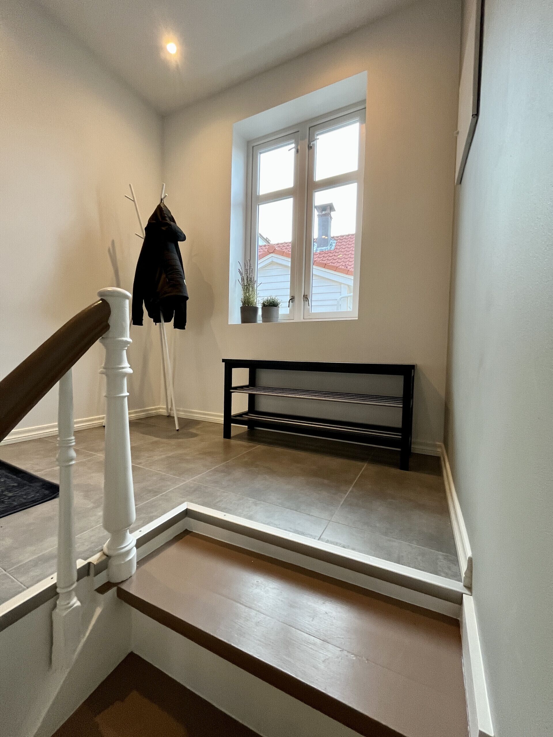 A staircase with a white railing, a bench, and a window with a view of a red-roofed building.