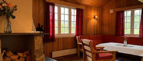 A wooden cabin interior with a dining table, chairs, a bench, and a fireplace.