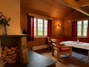 Interior de una cabaña de madera con una mesa de comedor, sillas, un banco y una chimenea.