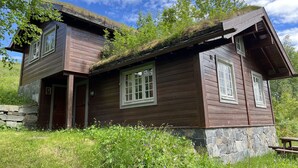 Eine Holzhütte mit Steinuntergrund, einem Schlafzimmer im Zwischengeschoss und einem Strohdach.