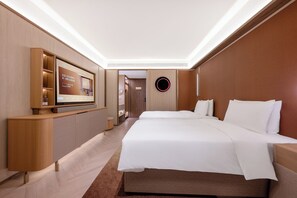 Habitación de hotel con una cama grande, un televisor montado en un mueble de madera y una lámpara de techo circular en la pared.