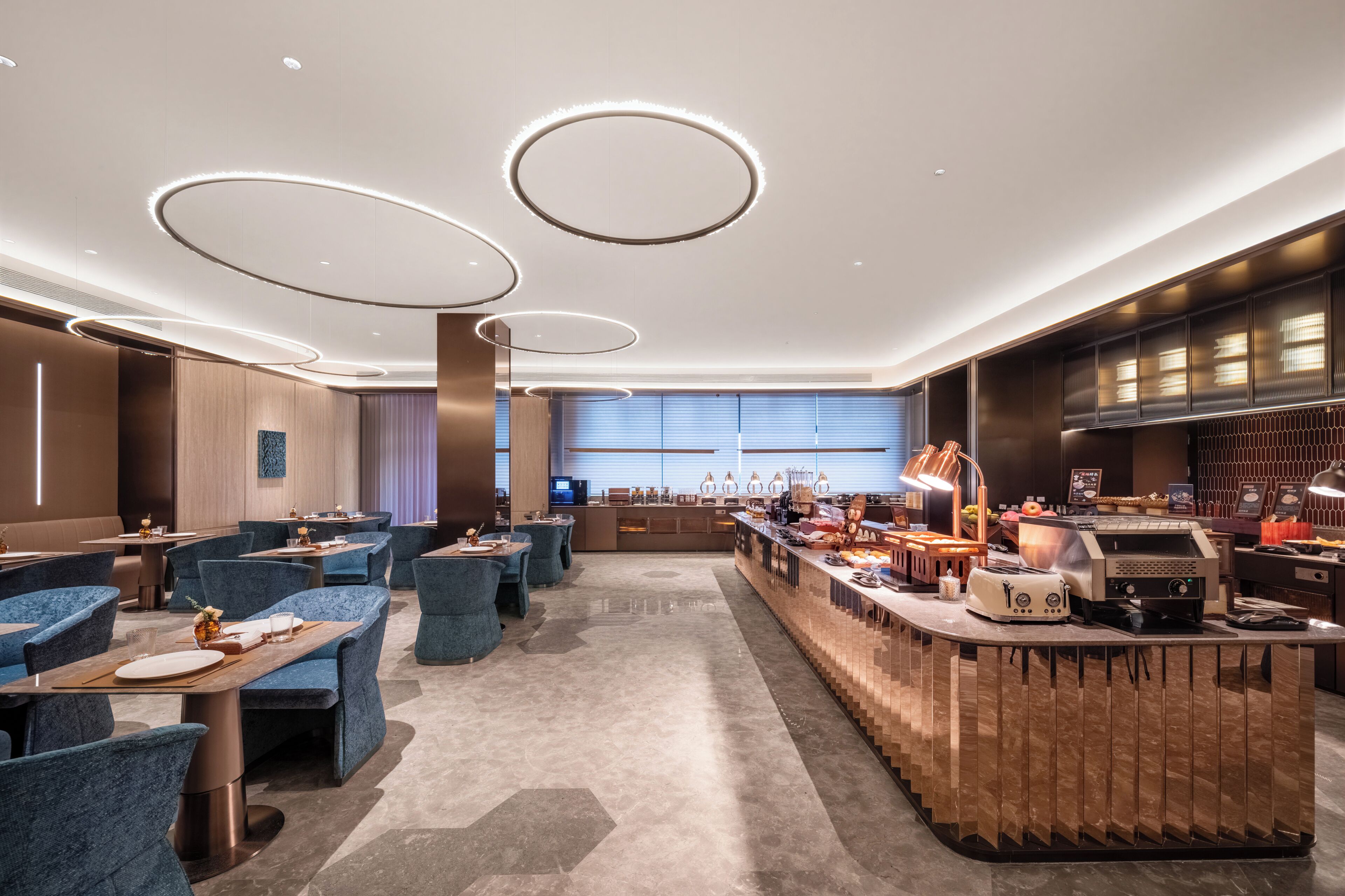 A modern restaurant with round ceiling lights, blue seating, and a counter with a coffee machine.