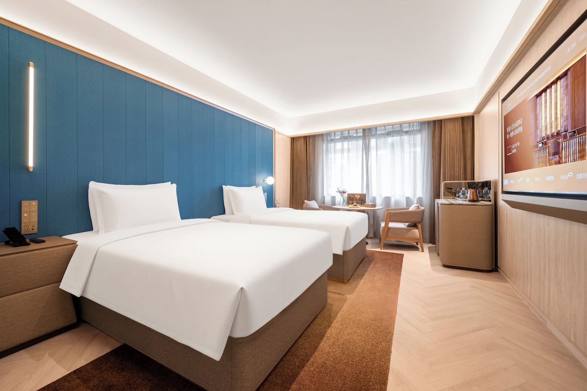 Habitación de hotel con dos camas, un escritorio, una silla, un televisor y un mini bar.