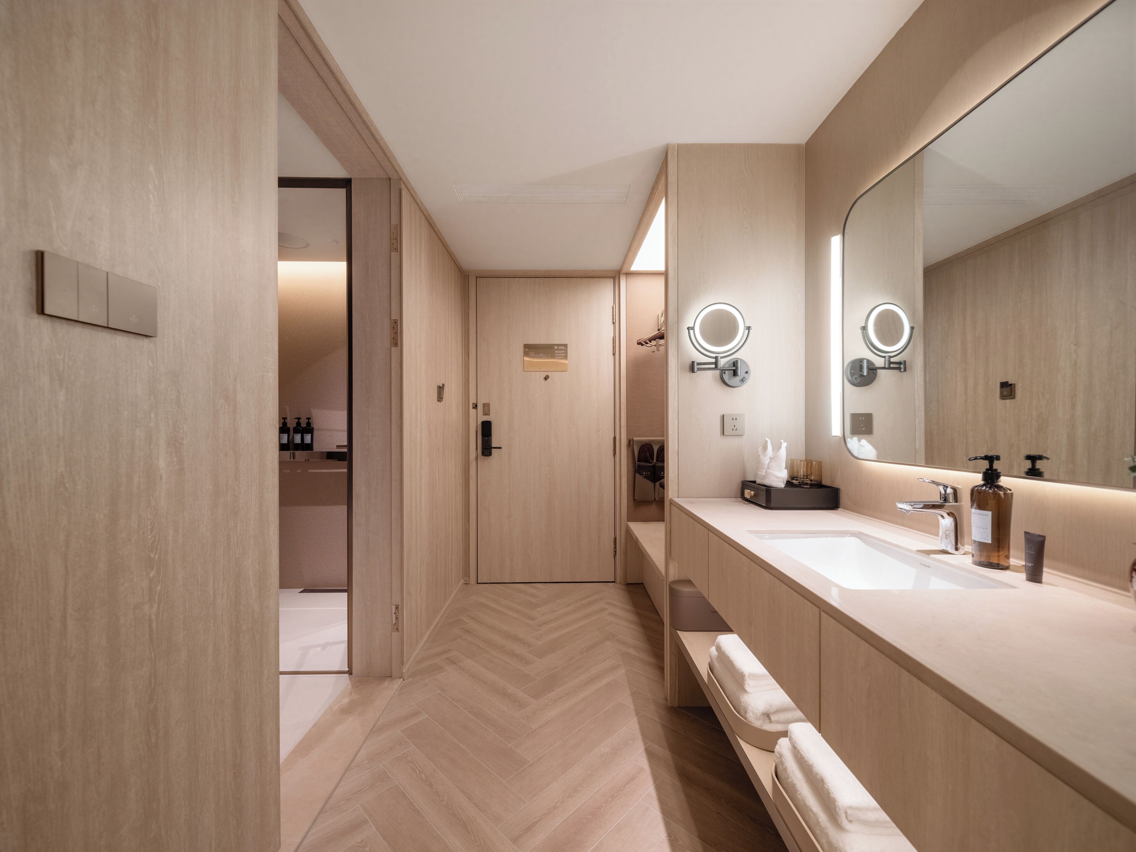Een moderne badkamer met een visgraatvloer, een wastafel met twee kommen en een grote spiegel met ingebouwde verlichting.