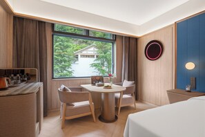 Habitación de hotel con zona de comedor, cama y vista a zonas verdes, además de un diseño de pared moderno.