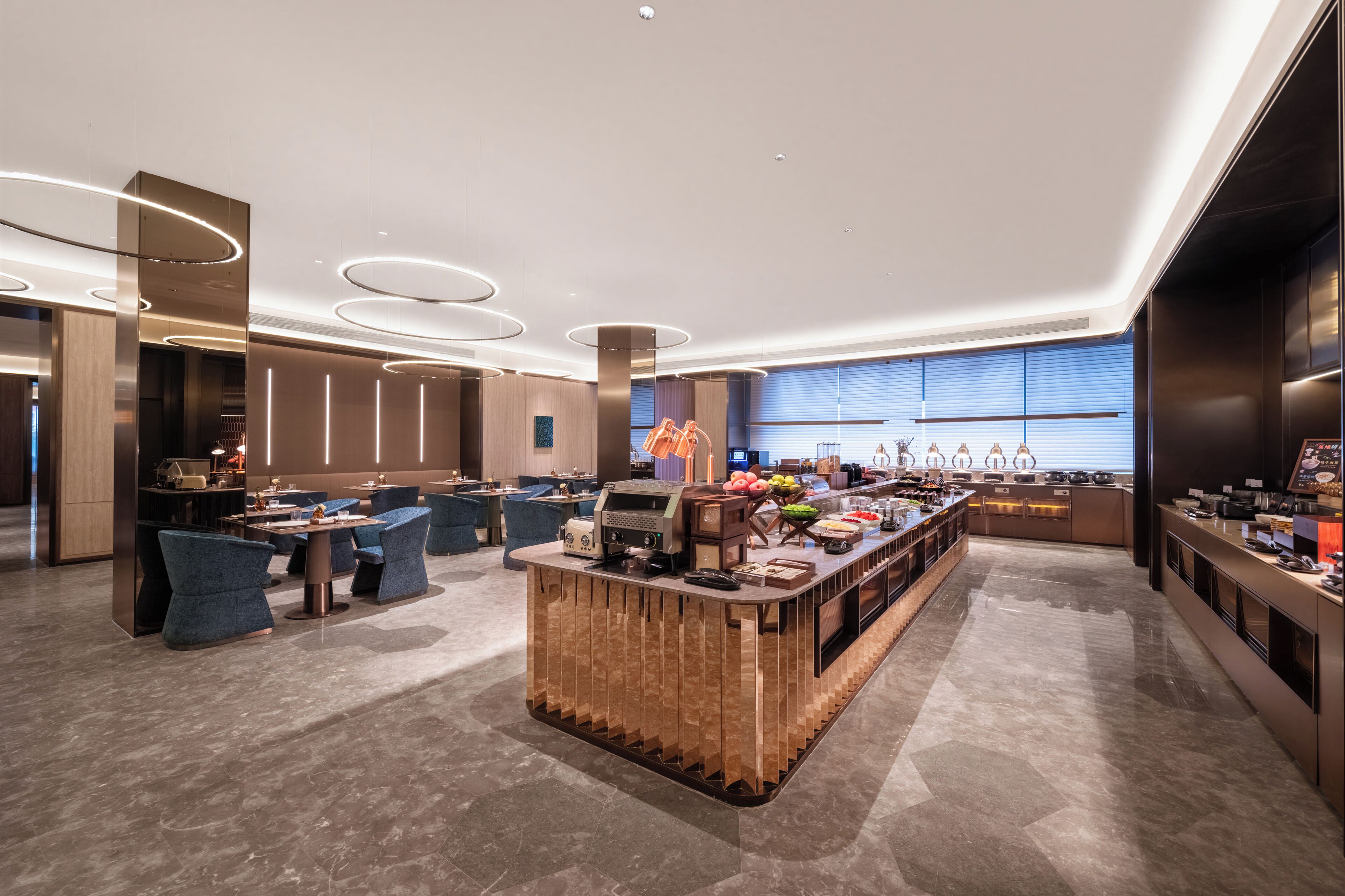 A modern hotel lobby with a central bar area, seating arrangements, and a large window providing natural light.