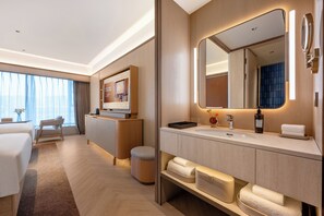 Una camera d'albergo moderna con un letto grande, un angolo salotto, una toeletta con specchio e vista sulla città.