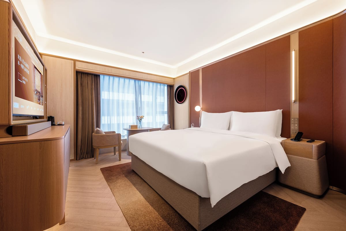 Habitación de hotel con una cama grande, un escritorio, una silla, un televisor y una ventana con cortinas.