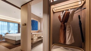 Una habitación de hotel moderna con una cama, un baño y un armario con ropa colgada y un paraguas.
