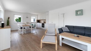 A modern kitchen with white cabinets, a dining area with a wooden table and chairs, a black leather sofa, and a small framed picture on the wall. - Holiday Apartment 'Bi Mimi' with Private Terrace and Wi-Fi (Nordstrand)