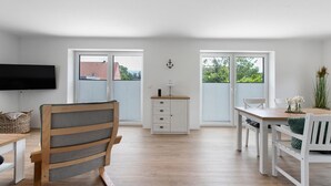 A modern kitchen with a dining area, wooden flooring, white cabinetry, and a flat-screen TV mounted on the wall. - Holiday Apartment 'Bi Mimi' with Private Terrace and Wi-Fi (Nordstrand)