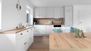 A modern kitchen with white cabinets, a wooden countertop, and a dining table with a vase of flowers. - Holiday Apartment 'Bi Mimi' with Private Terrace and Wi-Fi (Nordstrand)