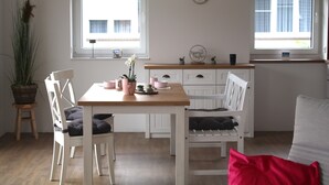 A room with a wooden dining table, white chairs, a small potted plant, and a red pillow on a white sofa. - Holiday Apartment 'Bi Mimi' with Private Terrace and Wi-Fi (Nordstrand)