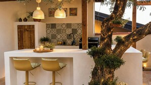 Een moderne keuken met een centraal kookeiland, barstoelen en een boom met verlichting.