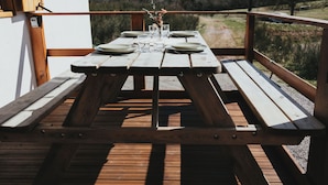 Un conjunto de mesa y sillas de madera para picnic al aire libre, con platos, vasos y un florero con flores.