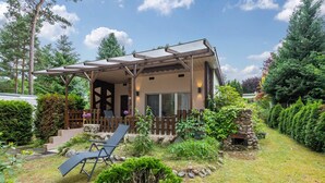 Une maison avec un porche abrité, une cheminée en pierre et un jardin avec un fauteuil de jardin.